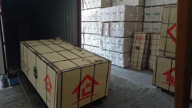 Carga en huacal de madera saliendo de un contenedor, junto a estibas de tablero resguardadas en el almacén